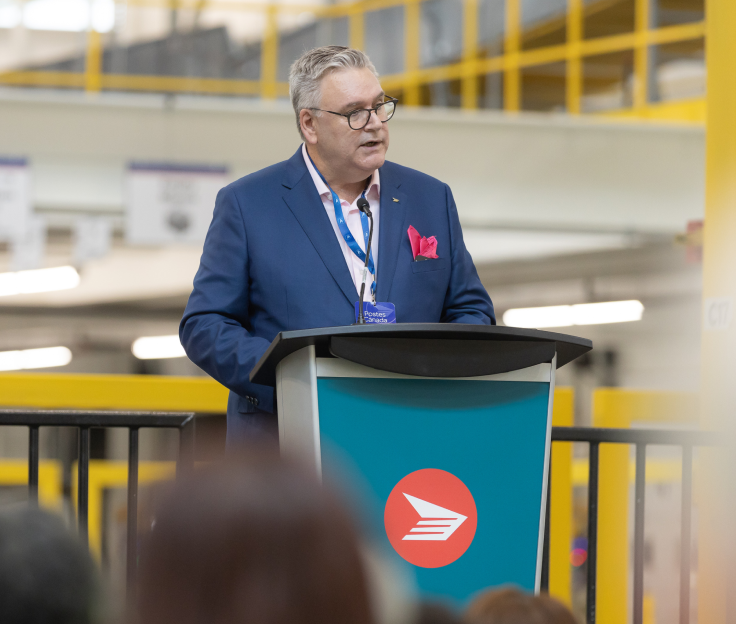 Canada Post President and CEO, Doug Ettinger stands at a podium speaking inside the new Albert Jackson Processing Centre.