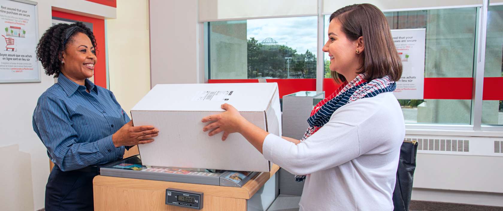 A post office clerk hands a package to a woman picking up her online purchase at her local Canada Post counter.