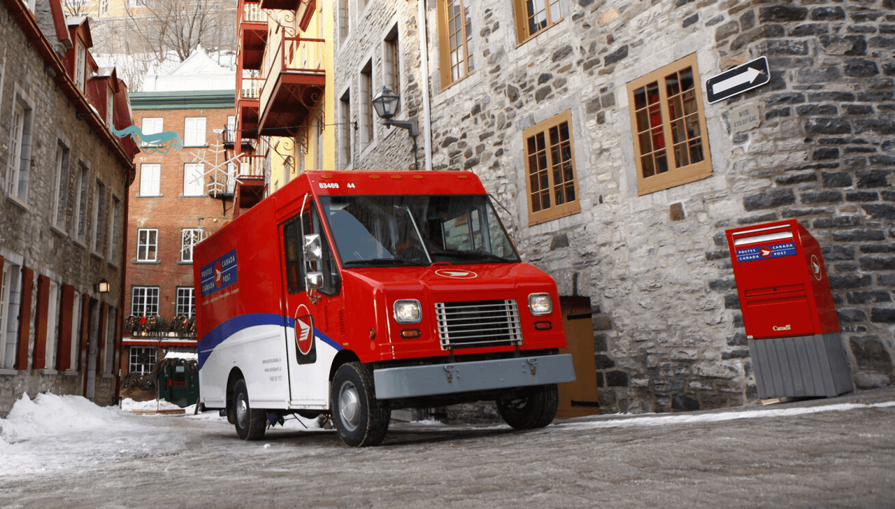 Une camionnette de Postes Canada est stationnée à côté d’une boîte aux lettres publique.