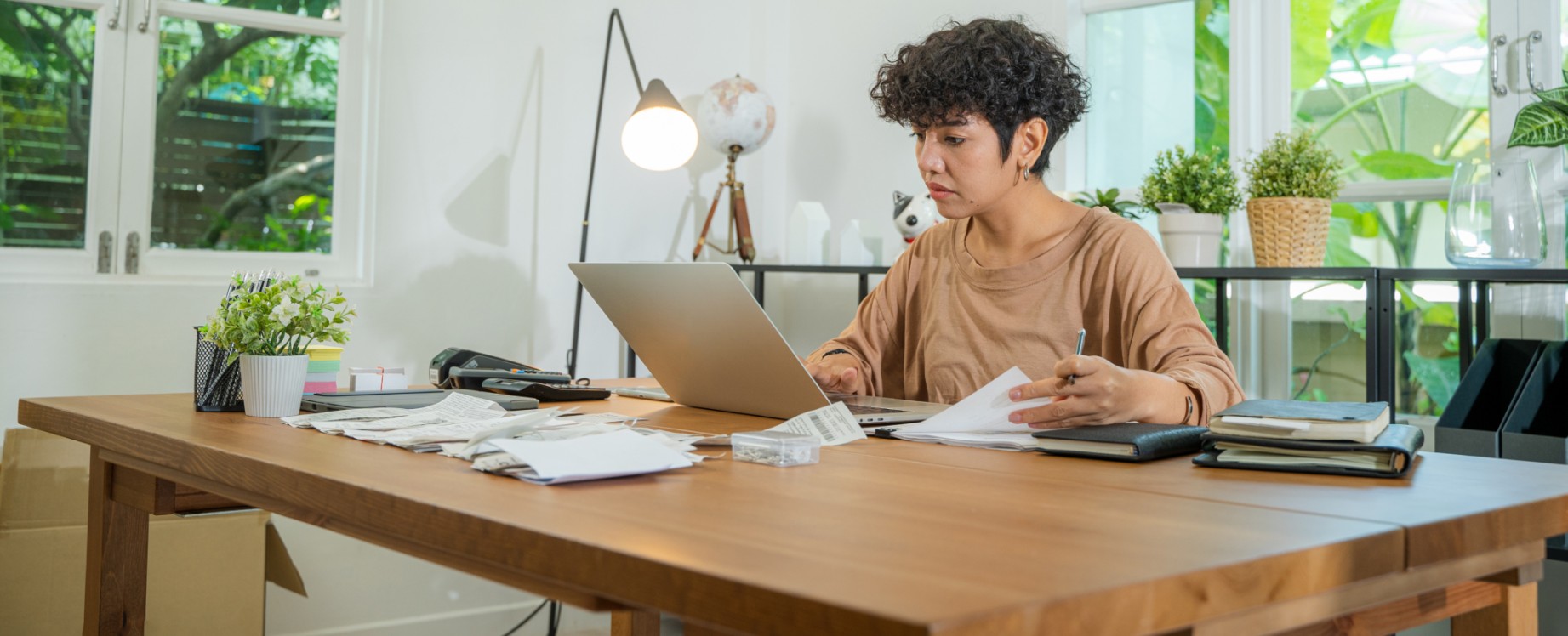 Une femme est assise à un bureau où elle travaille sur un ordinateur portable en feuilletant des documents.