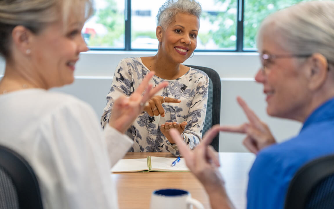 Trois femmes souriantes assises à une table ont une conversation en langage gestuel.